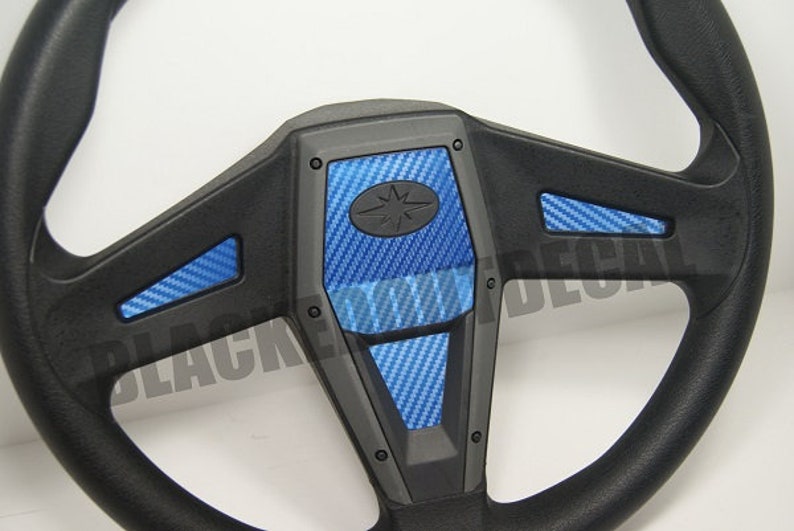May include: Black steering wheel with blue carbon fiber accents. The steering wheel has a star-shaped logo in the center.
