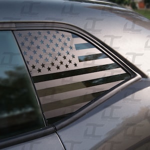 May include: A gray car with a black and white American flag decal on the rear quarter window.