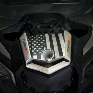 May include: A black and white American flag decal with the words "TURBO R" on the side. The decal is applied to the hood of a silver vehicle.