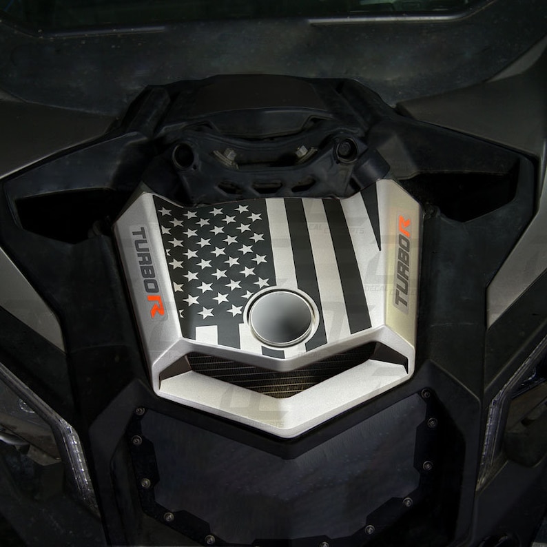 May include: A black and white American flag decal with the words "TURBO R" on the side. The decal is applied to the hood of a silver vehicle.