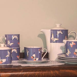 May include: A purple and white tea set with a butterfly design. The set includes a teapot, creamer, sugar bowl, and four cups.