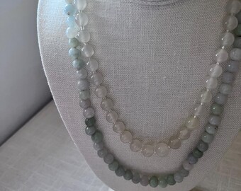 May include: Two strands of beaded necklaces displayed on a white bust. The beads transition in color from light blue to pale green and pink. The necklaces are made of round, polished beads.