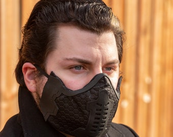 May include: A person wearing a black face mask with a honeycomb pattern. The mask has a geometric design and is made of a textured material.