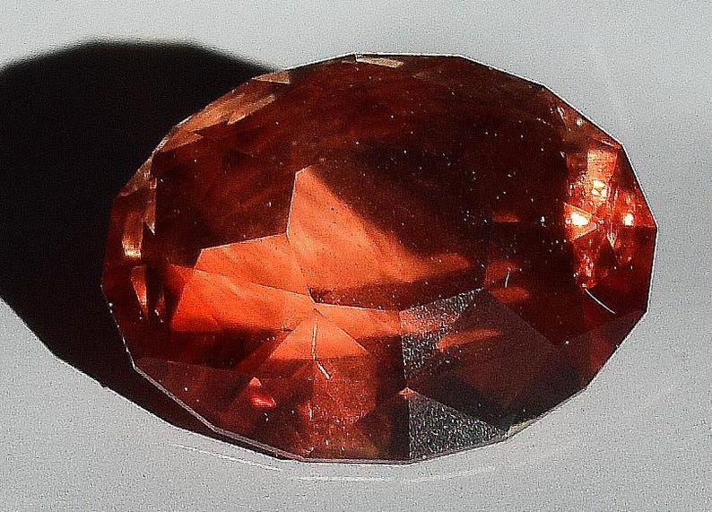 May include: A large, faceted, reddish-brown gemstone with a smooth, polished surface.
