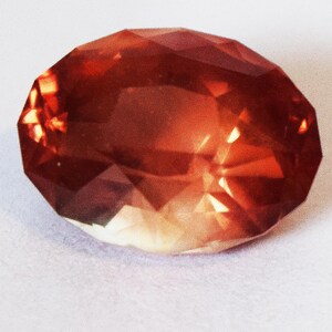 May include: A large, faceted, red-orange gemstone with a slightly cloudy appearance.