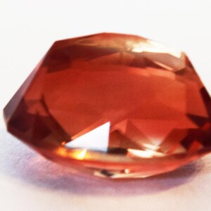 May include: A faceted, reddish-orange gemstone with a slightly irregular shape.