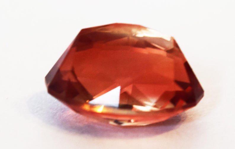 May include: A faceted, reddish-orange gemstone with a slightly irregular shape.