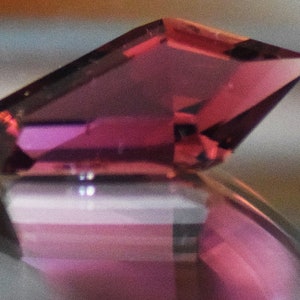 May include: A close-up of a pink gemstone with a faceted cut. The gemstone is set in a ring with a silver band.