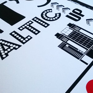 以下が含まれることがあります： 「I &hearts; BATIC」というテキストと、スタイリッシュな建物のイラストが描かれた白黒のグラフィックプリント。テキストは太字で、文字の周りに白い点が付いています。建物は、窓がたくさんある背の高い長方形の構造です。右と下に指し示す矢印があります。