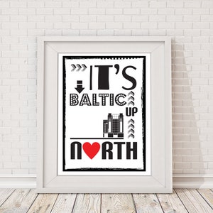 以下が含まれることがあります： 「It's Baltic Up North」というテキストが書かれた白黒のタイポグラフィー印刷。赤いハートが「North」の「O」を置き換えています。