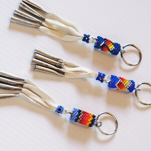 May include: Three beaded keychains with white leather tassels and silver metal accents. Each keychain features a blue, red, yellow, and black beaded cylinder with a silver metal key ring.