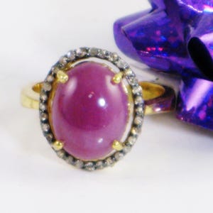 May include: A gold ring with a large oval ruby gemstone surrounded by a halo of small diamonds.