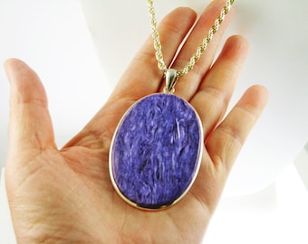 May include: A silver oval pendant with a purple and blue gemstone. The pendant is on a gold rope chain.
