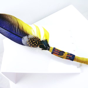 May include: A blue, yellow, and black feather with a beaded wrap. The beads are blue, red, and yellow.