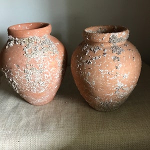May include: Two terracotta pots with a rough, textured surface. The pots are a light brown color and have a white, speckled pattern.