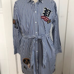 May include: A blue and white striped shirt dress with a tie belt and various patches. The patches include a large "R" with a crown, a "Game Ward" patch, and a patch with Japanese characters.