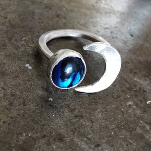 May include: A silver ring with a blue and black cabochon stone and a crescent moon design.