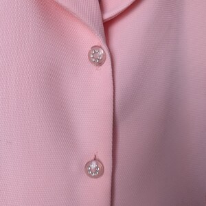 May include: A pink blazer with two decorative buttons. The buttons are round and have a silver finish with small rhinestones.