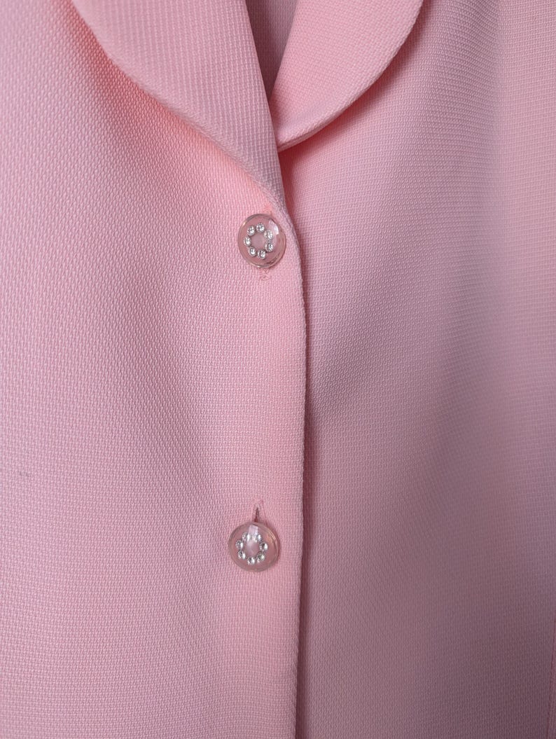 May include: A pink blazer with two decorative buttons. The buttons are round and have a silver finish with small rhinestones.
