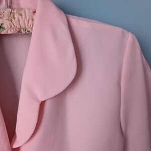May include: A pink collared blouse with a rounded collar. The collar is folded over and has a scalloped edge.