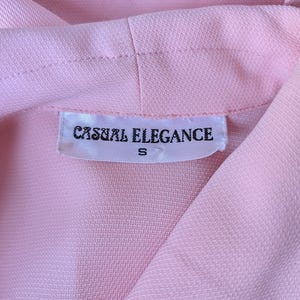 May include: A pink blouse with a white tag that reads "Casual Elegance" and "S" in black text.