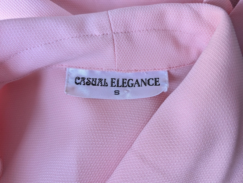 May include: A pink blouse with a white tag that reads "Casual Elegance" and "S" in black text.