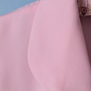 May include: A close-up of a pink blazer with a textured fabric. The blazer has a notched collar and a single button closure.