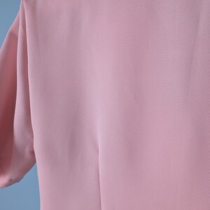 May include: A pale pink, short-sleeved, lightweight top made of a textured fabric.