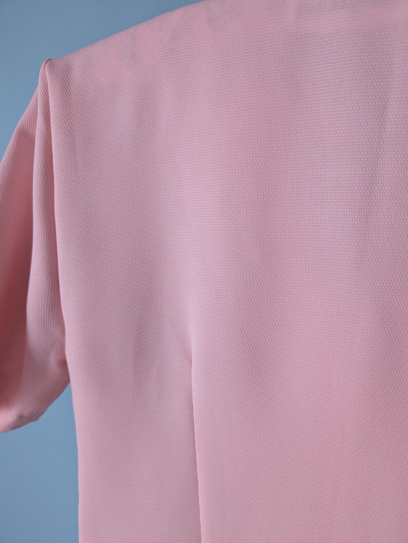 May include: A pale pink, short-sleeved, lightweight top made of a textured fabric.