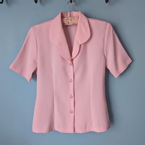 May include: A pale pink short-sleeved button-up blouse with a collar.