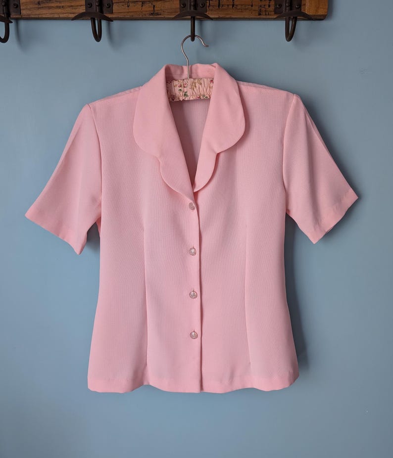 May include: A pale pink short-sleeved button-up blouse with a collar.