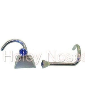 May include: Two nose rings with blue gemstones. One is a curved nose stud with a round blue gem, and the other is a straight nose stud with a similar blue gem. The jewelry is silver-toned.