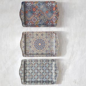 May include: Three rectangular serving trays with raised edges, each featuring a distinct intricate geometric and floral pattern in shades of blue, orange, red, and cream. The trays are arranged vertically, showcasing varied repeating designs.