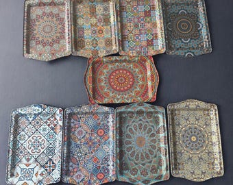 May include: A collection of decorative serving trays with ornate, colorful patterns. The trays feature a rectangular shape with curved edges and a variety of geometric and floral designs in shades of red, blue, green, and gold. The trays are arranged on a dark surface.