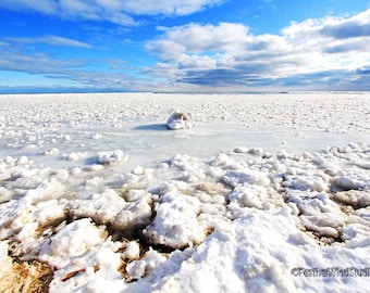 Puede incluir: Un paisaje invernal de un lago congelado bajo un cielo azul brillante con nubes dispersas. El primer plano presenta grandes trozos de hielo y nieve, que se transforman en una vasta extensión de hielo blanco en la distancia.