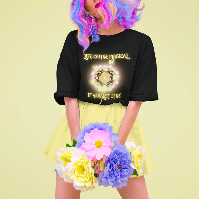 May include: A black t-shirt with a dandelion graphic and the text "Life can be magical if you let it be". The model is wearing a yellow skirt and holding a bouquet of flowers.