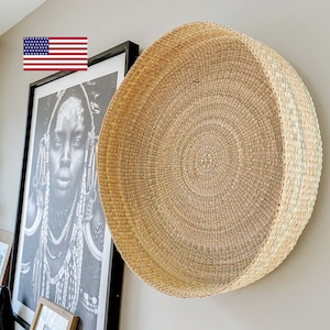 May include: A large, round, woven wall decor piece made of natural materials. The decor is light brown and beige in color and has a circular pattern.