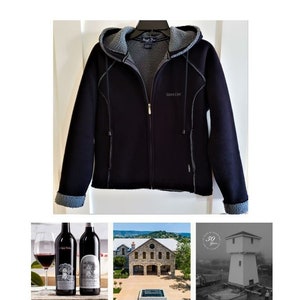 May include: A black fleece jacket with a hood and zipper closure. The jacket has a gray fleece lining and the brand name "Silver Creek" is printed on the front. Two bottles of wine are shown in the image, along with a glass of wine and a building with a stone facade.