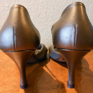 May include: A pair of bronze-colored high-heeled shoes. The shoes have a pointed toe and a thin, curved heel. The heels are approximately 3 inches tall.