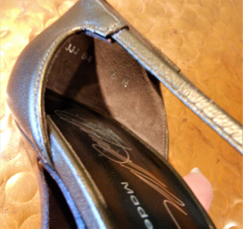 May include: Close-up of a metallic silver high-heeled shoe. The shoe has a strap and a pointed toe. The interior of the shoe is dark brown, with the size marked as 6 M. The text "JJJ 54" is visible.