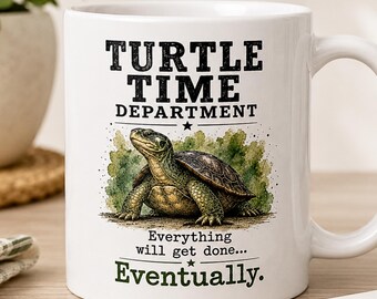 May include: A white ceramic mug featuring a green turtle illustration and black text that reads TURTLE TIME DEPARTMENT Everything will get done... Eventually. The design includes a watercolor-style green background behind the turtle.