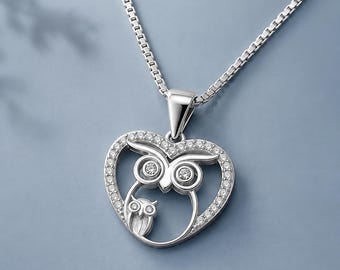 May include: A silver-toned necklace featuring a heart-shaped pendant with a pavé-set border. Inside the heart, a large owl figure with crystal-accented eyes stands beside a smaller owl figure. The pendant hangs from a delicate box chain.