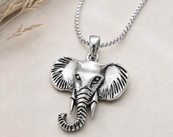 May include: A silver-toned metal necklace featuring a detailed elephant head pendant with large ears, a curved trunk, and two tusks. The pendant is suspended from a thin, polished silver-colored box chain that connects to a small metal bail.