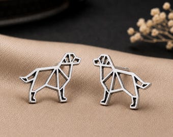 May include: A pair of silver-toned stud earrings featuring a geometric, wireframe-style dog silhouette. The metal has a darkened, oxidized finish within the recessed lines, creating a clear outline of a canine shape with a pointed tail and ears.