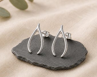 May include: A pair of silver-toned wishbone stud earrings with a polished metallic finish. Each earring features a curved, Y-shaped design with a standard post backing, presented as a matching set of two individual jewelry pieces.