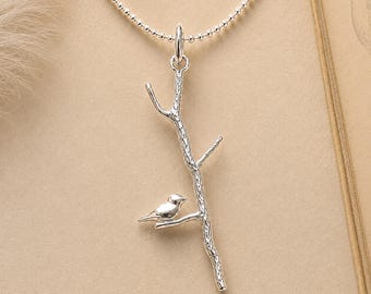 May include: A silver necklace featuring a pendant shaped like a textured tree branch with a small bird perched on one of the limbs. The pendant hangs from a delicate silver ball chain, showcasing a polished metallic finish and intricate details.