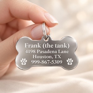 May include: A silver-toned, bone-shaped metal pet ID tag featuring engraved text that reads Frank (the tank), 4198 Pasadena Lane, Houston, TX, 999-867-5309, accompanied by two small paw print icons with heart-shaped centers on the bottom corners.