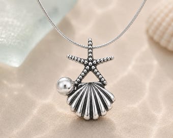 May include: A silver-toned necklace featuring a pendant with a textured starfish resting atop a ribbed seashell, accented by a single smooth, round silver bead. The pendant hangs from a thin, flexible silver-toned snake chain necklace.