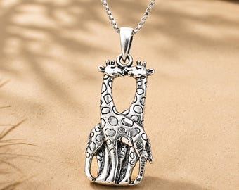 May include: A silver-toned metal pendant necklace featuring two giraffes standing side-by-side with their necks curved toward each other. The pendant has a detailed cutout design with dark oxidized accents highlighting the giraffe spot patterns.