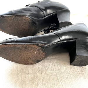 May include: A pair of black leather heeled shoes with lace-up closures. The shoes have a rounded toe and a block heel.